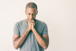 Calm spiritual handsome African guy praying with closed eyes